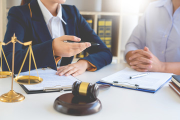 Two people in formal attire sit at a desk with legal documents, a gavel, and a balance scale, discussing how family businesses are divided during divorce in a bright office setting.